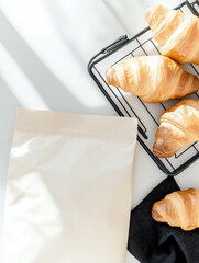 Freshly baked croissants arranged on a cooling rack with a blank packaging mockup beside them