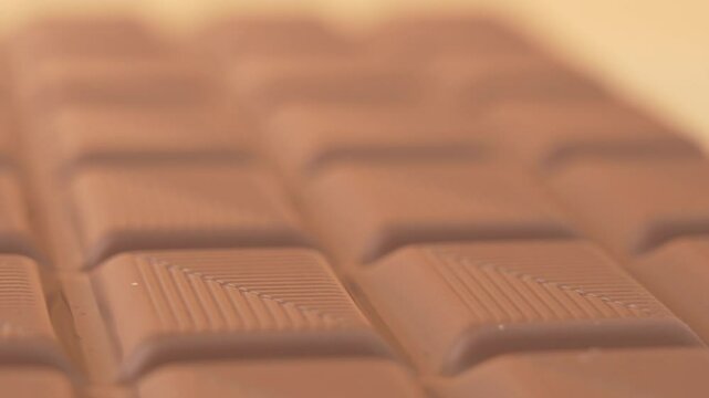 Close-up of a brown chocolate bar. The concept of enjoyment and pleasure, as chocolate is often associated with comfort and happiness. The close-up highlights the texture. Chocolate rotates on an oran