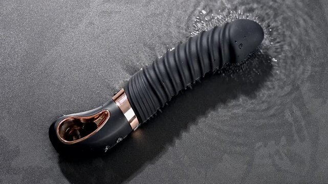 Black silicone vibrator in water. Circles on water around sex toy. 