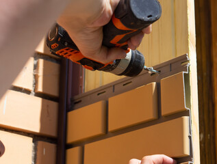 a guy is covering a house with plastic panels, screwing a screw with a screwdriver