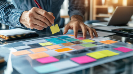 Close-Up Shot of Professional Hands Arranging Vibrant Sticky Notes on Transparent Glass Board, Brainstorming Ideas for New Product Launch in Open-Plan Office with Collaborative Atmosphere