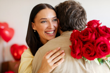 Happy Valentine's Day. Man giving bouquet of red roses to his beloved woman, lady embracing husband...