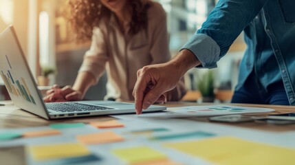 Close-up of colleagues brainstorming on a laptop with charts and post-it notes in a modern tech startup environment