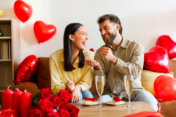 Happy Valentine's Day. Couple in love eating cakes, sitting on sofa in decorated room and...