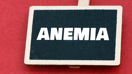 ANEMIA word on a small chalk board next to a stethoscope on a red background.