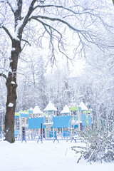 A vibrant childrens playground surrounded by snow-covered trees in a peaceful winter park. The...