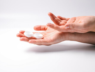 Hands holding a contact lens and an open lens case on a white background. Concept of eye care, hygiene, and vision correction