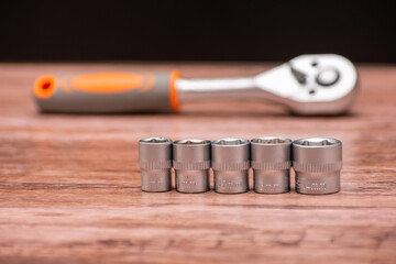 Set of five metal sockets of different sizes is neatly arranged in a row on a wooden surface, with...