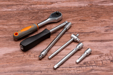 Set of socket wrench holders, a screwdriver with attachments, and various socket extensions are laid out on a wooden surface, showcasing the versatility and functionality of the tools.