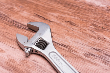 Silver adjustable wrench lying on a wooden surface. The wrench is open, suggesting recent use. The polished metal contrasts with the natural wood grain beneath.