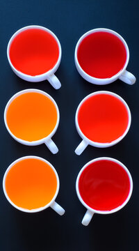 Six white cups with cherry, strawberry and orange sweet dessert jelly, installed on a black surface, view from above, vertical image