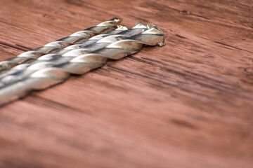 Drill bits neatly arranged on a wooden surface. Metallic finish of bits contrasts with natural wood...