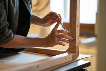 Carpenter hands use hex key to screw bolts, attaching table legs to wooden tabletop in workshop....
