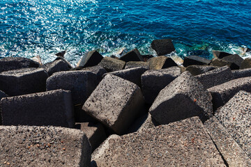 Shaped concrete blocks arranged along shoreline, with ocean water visible in background. Blocks are used as breakwaters to protect coast from waters force. Coastal engineering erosion control methods