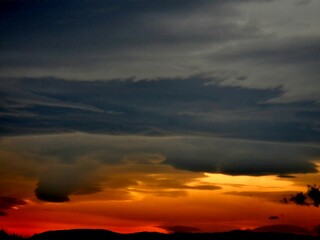 Dark cloudy sky with grey and red color, effect of burning sky over black horizon with mountains during sunrise on windy weather. Topics: air space, meteorology, atmosphere, abstraction, wallpaper
