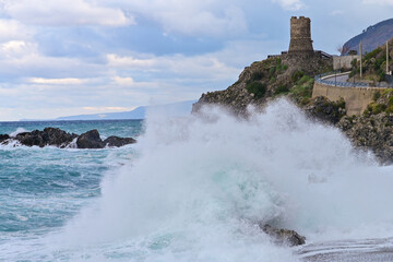 Onda del mare che si infrange su una roccia e Torre antica sullo sfondo