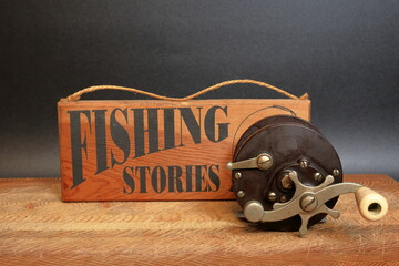 Wooden fishing stories sign beside a classic fishing reel, on a wooden board, before a black...
