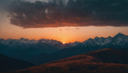 Sunset over majestic mountain range with rolling hills in the foreground and dark clouds above during late evening hours