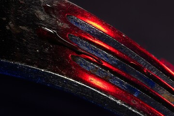 Abstract of tines of a chrome fork with red and blue reflections and a drop of water