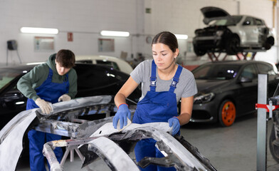 Female mechanic prepares car for painting in workshop - grinds and puts putty on the bumper before...