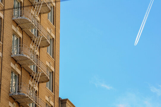 Vintage brick apartment with fire escapes and jet contrail in blue sky