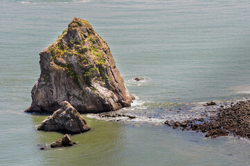 Coastal rock formations rise from the ocean along a tranquil shoreline