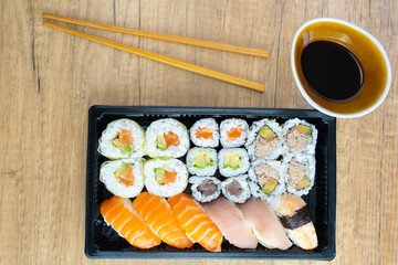 Sushi to go combo in black box with wooden chopsticks on elegant wooden table background with space for copying, and bowl with soybeans. Home delivery concept.
