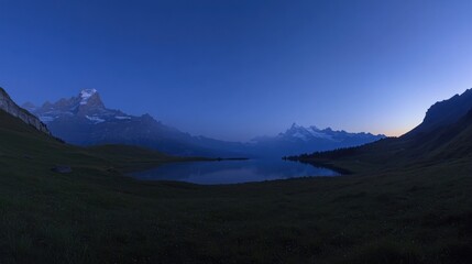 Obraz premium Serene twilight landscape with a tranquil lake reflecting majestic snow-capped mountains under a deep blue sky.