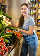 Young woman chooses zucchini for purchase in greengrocer shop