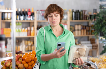 Checking expiration date of canned food - female shopper scans code with her smartphone on the label of fresh oyster mushrooms
