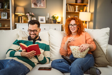 Obraz premium cheerful couple enjoy together on sofa with book and popcorn