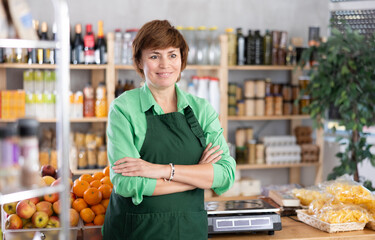 Portrait of female seller in an apron behind the counter of a grocery store