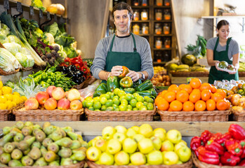Male salesman near fruit and vegetables stalls offering to buy green peppers