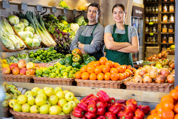 Male and woman salespeople standing near market stalls offering to buy fruits and vegetables