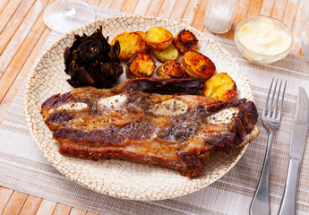 Fresh grilled beef rib steak, churrasco de ternera, served on table with roasted potatoes and artichoke.