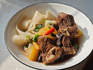 fresh beef stew with potatoes on the wide noodles in the bowl for eating