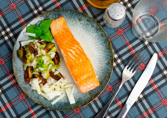Hearty and dietary lunch is served: fried salmon fillet, green Mexican guacamole pate, slices of cheese and slices of tomatoes. Food is served on simple wooden lacquered table