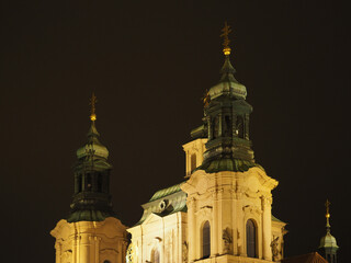 Ornate church towers with golden spires and domes lit up against dark night sky. Prague, Czech Republic