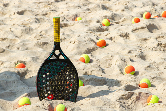 Raquete de beach tennis em p&eacute; na areia cercada por bolas para  o jogo
