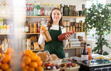Teenage girl seller at counter offering tomato and peach juices in grocery store