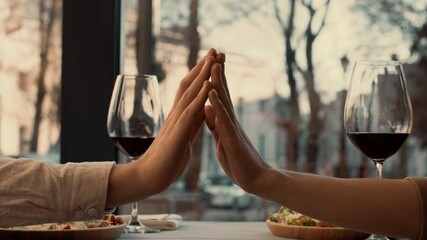 A couple shares a romantic dinner, their hands almost touching, with two glasses of red wine and a salad. The intimate setting highlights their connection amid a warm ambiance.