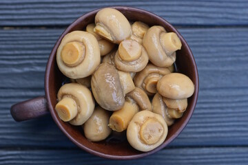 gray small canned champignon mushrooms in a brown ceramic cup stands on a black wooden table