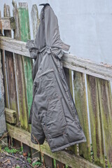 one green hooded fabric jacket hanging on grey wooden fence on autumn street