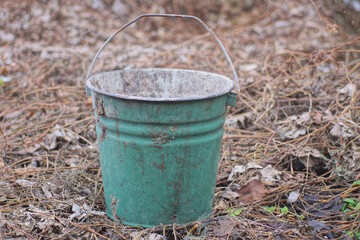 one old big green dirty metal bucket stands on the street on gray dry vegetation in the street © butus