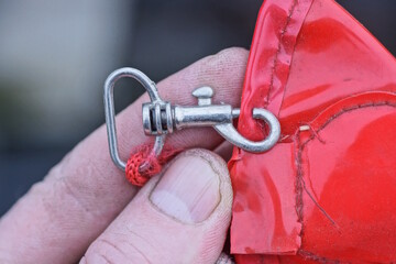 hand holding small grey metal carabiner clasp on red leather bag