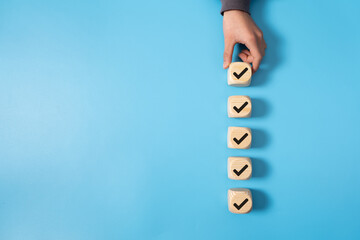 Wooden blocks with checkmarks arranged in a vertical line, symbolizing completed tasks, progress tracking, or goal achievement, against a light blue background.