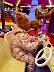 Happy little girl in warm red jacket and knitted reindeer hat riding carousel horse during family...