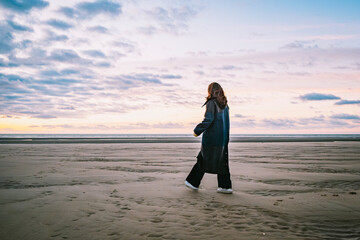 Women walking across the beach wearing a coat during sunset