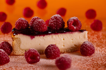 Delicious cheesecake topped with fresh raspberries and berry sauce against an orange backdrop