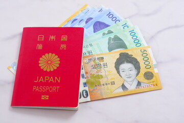 Fototapeta premium 韓国の通貨、ウォンKRWの紙幣とパスポート（一般旅券10年用赤色）を用意して、韓国への旅行を計画しているイメージ 